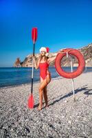 A woman in a red bikini and a Santa hat put her hand on a lifebuoy against the background of the sea, beach, rocks. The concept of holiday and travel. photo