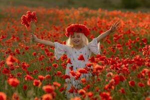 A young girl is standing in a field of red poppies, holding a bouquet of flowers. She is smiling and she is enjoying the beautiful scenery. Concept of joy and happiness photo