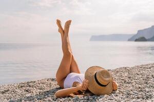 A woman is laying on the beach wearing a straw hat and a white bikini. She is enjoying the sun and the beach. photo