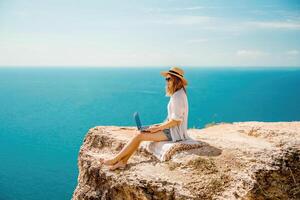 Freelance woman working on a laptop by the sea, typing away on the keyboard while enjoying the beautiful view, highlighting the idea of remote work. photo