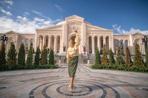 A woman in a long skirt and sweater poses in front of a large, ornate building with columns photo