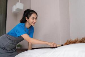 Asian housekeeper dusting a bed with a feather duster photo