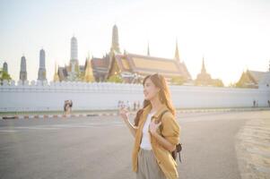 Traveler asian woman in her 30s, backpack slung over her shoulder, explores the intricate details of Wat Pra Kaew with childlike wonder. Sunlight dances on the golden rooftops. photo