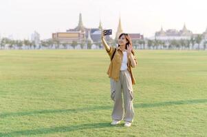 Traveler asian woman in her 30s take a livestream on smartphone while explores Wat Phra Kaew emerald Buddha. Share the wonders of Thai heritage through her journey. photo