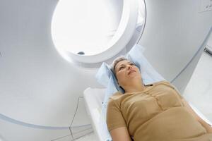 Female patient lying on table and entering CT machine during examination procedure in hospital photo