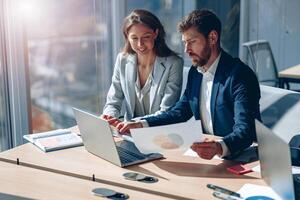 Two smiling business people in modern office explaining statistics data to each other photo