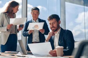Focused businessmen discussing work issues using laptop and documents with charts in a modern office photo