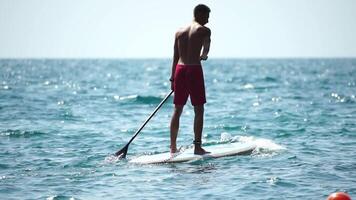 Man Sup Sea. Strong athletic man learns to paddle sup standing on board in open sea ocean on sunny day. Summer holiday vacation and travel concept. Aerial view. Slow motion video