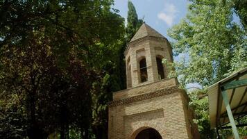 An ancient stone chapel, with a bell tower, is part of a medieval Georgian church dedicated to St. George. On top of the tower, a cross stands proudly against the blue sky. Slow motion video