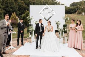 A bride and groom stand in front of a white wall with the letters J and F on it photo