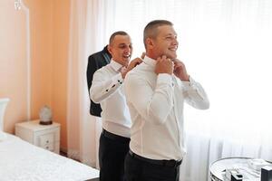 Two men are getting dressed up in a bedroom. One of them is wearing a suit and tie photo
