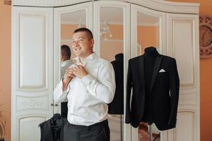 A man in a suit is standing in front of a mirror, getting ready for a formal event photo