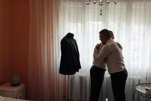 Two men hug each other in front of a mannequin wearing a black suit. The scene is intimate and warm, with the men embracing each other in a moment of closeness photo