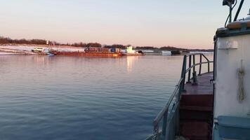 Boat floats on background of river cargo berth. Clip. View from floating boat to shore with pier. Boat sails to shore with barge on sunny winter day photo