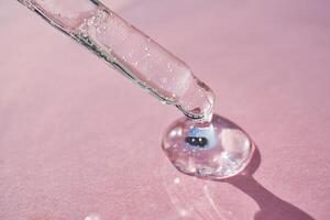 Pipette with serum shimmering in the sun on a pink background. photo