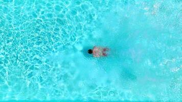 Aerial view as a man dives into the pool and swims. Slow motion video