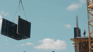 Construction crane lifting large panel on building site. A crane is seen lifting a large panel while a construction worker stands on an elevated platform. video