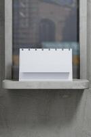 A white desk calendar sitting on a ledge with a window behind it photo