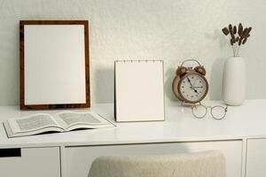 A blank desk calendar on a desk with glasses, alarm clock and a picture frame photo