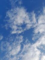 White clouds in the blue sky. Beautiful bright blue background. Light cloudy, good weather. Curly clouds on a sunny day. photo