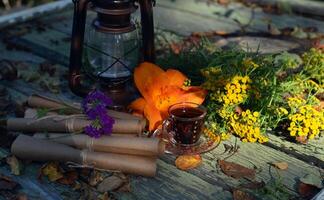 Mystic still life with old paper scrolls, lantern, flowers and witchy ritual objects on old table. Occult, esoteric, wicca and divination concept. photo