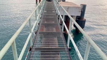 Metal walkway over the Sea. A metal walkway leading out over the sea, it has handrails on both sides and it is built on a wooden structure. In the background a mountain can be seen on the coastline. video