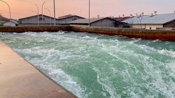 Rushing Water in Concrete Channel. Rapid water flows through a concrete channel, creating a powerful and turbulent current. The water is green and teal in color, with white foam and waves. video