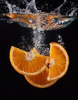 Orange slices falling into water at black background, splashes and bubbles of food photo