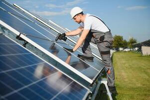 Side view of male worker installing solar modules and support structures of photovoltaic solar array. Electrician wearing safety helmet photo