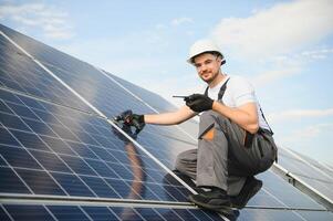 Side view of male worker installing solar modules and support structures of photovoltaic solar array. Electrician wearing safety helmet photo