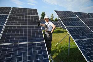Side view of male worker installing solar modules and support structures of photovoltaic solar array. Electrician wearing safety helmet photo