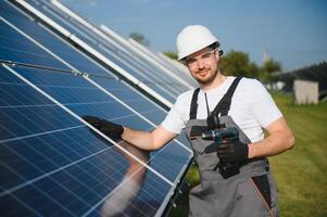 Side view of male worker installing solar modules and support structures of photovoltaic solar array. Electrician wearing safety helmet photo