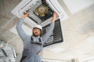 Indian male worker inspecting the air conditioner mounted on the ceiling photo