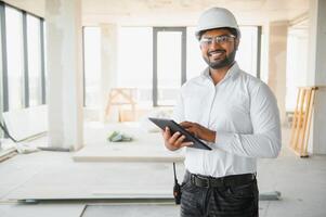 Indian construction site manager standing wearing helmet, thinking at construction site. Portrait of mixed race manual worker or architect photo