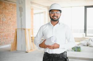 Indian construction site manager standing wearing helmet, thinking at construction site. Portrait of mixed race manual worker or architect photo