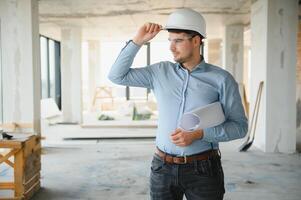 Portrait of an architect builder studying layout plan of the rooms, civil engineer working with documents on construction site photo