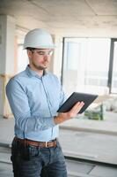 Supervisor standing in building in construction process, holding tablet and checking on works photo