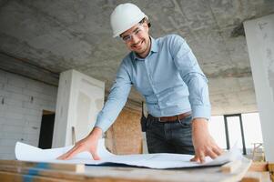 Portrait of an architect builder studying layout plan of the rooms, civil engineer working with documents on construction site photo