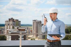 Supervisor standing in building in construction process, holding tablet and checking on works photo