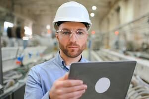 Engineer in hardhat is using a laptop in a heavy industry factory photo