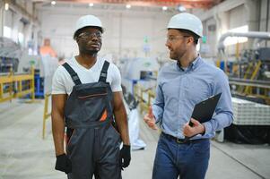 Two Diverse Professional Heavy Industry Engineers Wearing Safety Uniform and Hard Hats Working on Laptop photo