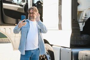 Truck driver standing by his truck and talking on the phone. Man driver getting in touch with his family photo