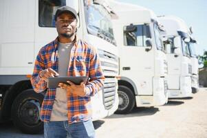 African American professional truck driver setting up navigation for destination. Checking his route on tablet computer and standing by long vehicle. Transportation service photo