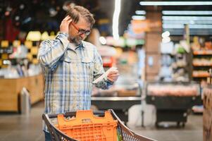 Minded man viewing receipts in supermarket and tracking prices photo