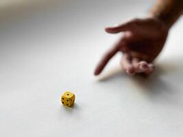 Hand preparing to roll yellow dice on minimalist white background photo
