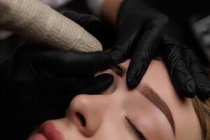 An experienced beauty professional is focused on meticulously shaping a client's eyebrows using specialized tools, ensuring a flawless look. The client appears relaxed as the treatment is performed. photo