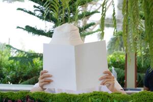 Close up and selective focus hands of teenage girl holding and reading book or magazine and sitting in chair at garden of home. photo