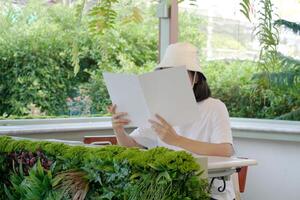 Close up and selective focus hands of teenage girl holding and reading book or magazine and sitting in chair at garden of home. photo