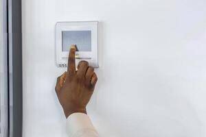 African American businesswoman uses modern digital thermostat to manage office temperature. Image depicts hand interacting with sleek device on wall, showcasing smart technology in workplace photo