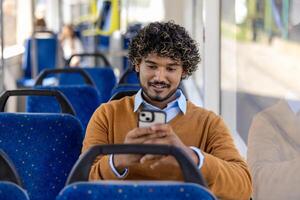 Man sitting on bus using smartphone with a smile. Casual setting in public transport with blue seats and window light. Engaged and relaxed moment captured. photo